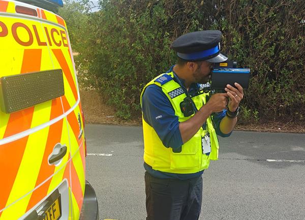 A police community support officer using a speed gun stood beside a police van