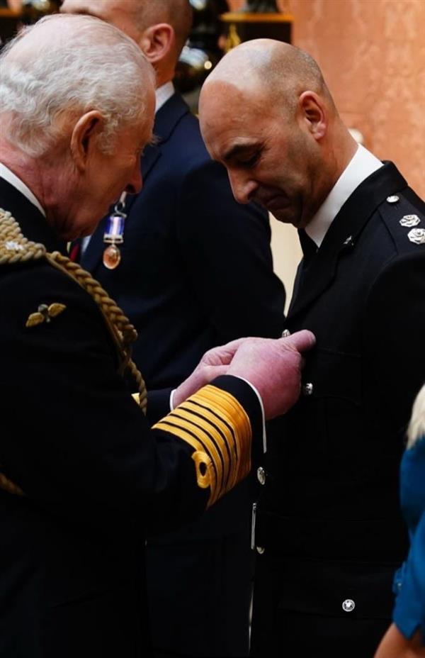 Shammi stood in a line with King Charles pinning a medal to his chest. Both are in full uniform.