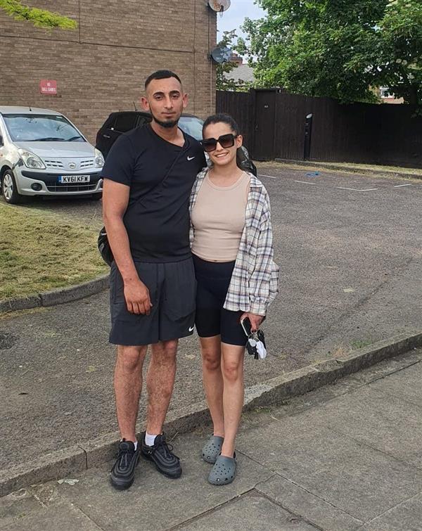 Natasha and Karlo stood together smiling, in a small carpark.