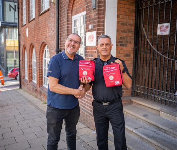 Two men posing shaking hands holding bleed kits