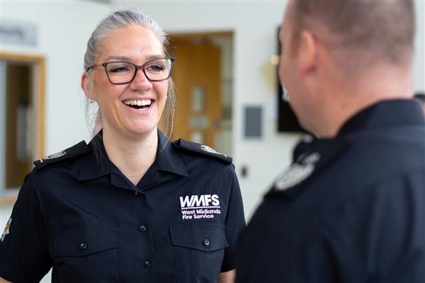 A female colleague wearing glasses, and the new uniform shirt, laughing and smiling while talking to a male colleague.