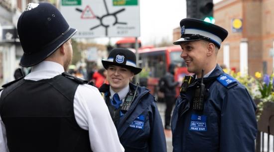 Two Police Community Support Officers talking to a Police Officer wearing a police helmet.