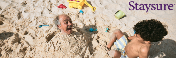 Image shows a man buried in sand on holiday.