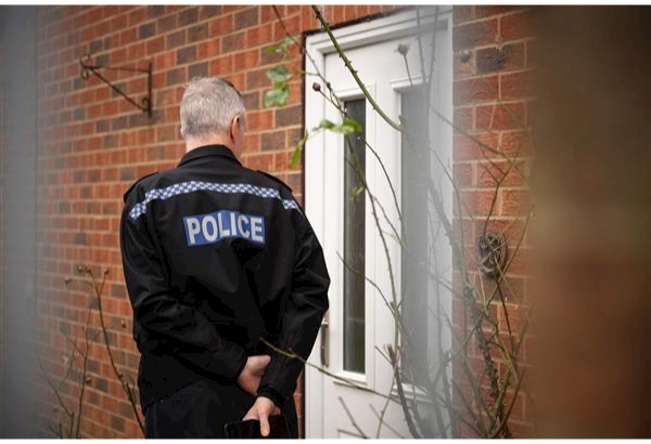 Officer in uniform stands at a residential door which is white.