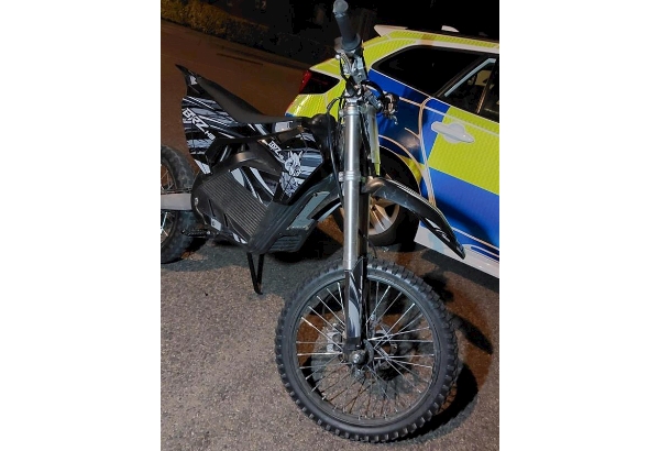 Image is of a black electric bike that was seized during this incident, the bike is in front of a police vehicle.