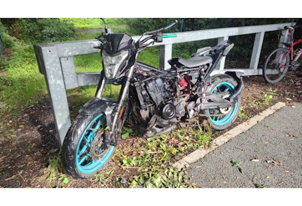 Poor condition Motorcycle With Blue Wheels leaning against galvanised barrier.