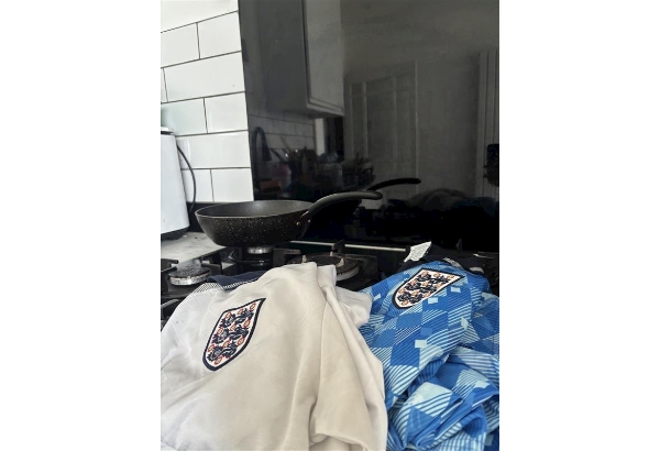 Two England football shirts on a gas hob that has a frying pan on. 
