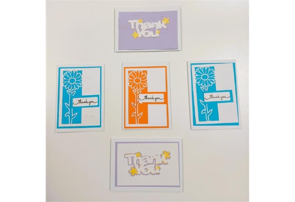Five handmade thank you cards displayed on a white surface. Two cards feature layered “Thank You” text in white and yellow on a lilac background, positioned at the top and bottom. Three cards in the centre row feature decorative floral designs, with two in turquoise and one in orange, each containing a small label reading “thank you.” The cards are neatly arranged in a cross-like pattern, showcasing colourful, handcrafted paper-cut designs.